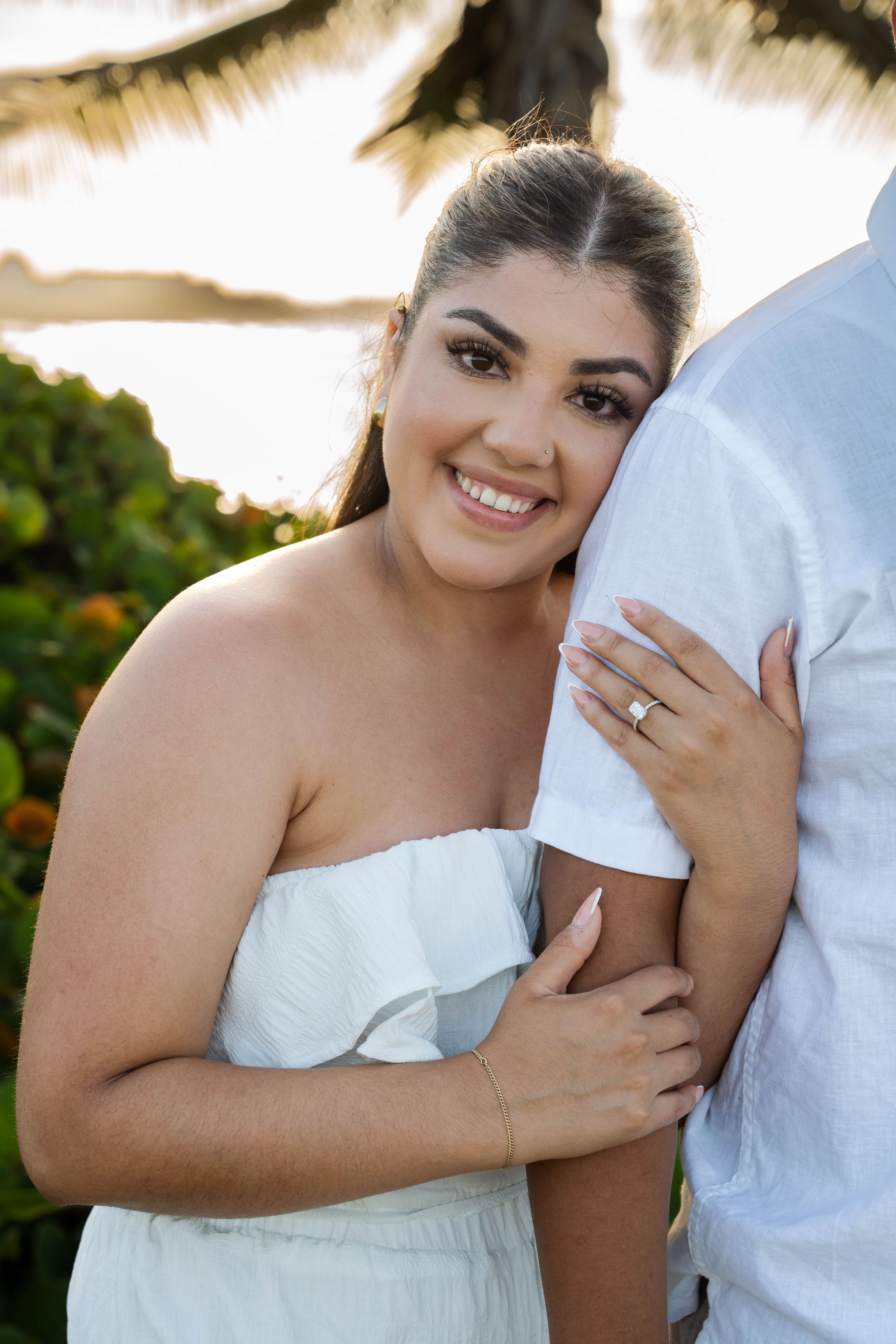 Happy couple posing for engagement photos at a tropical beach location with palm trees.
