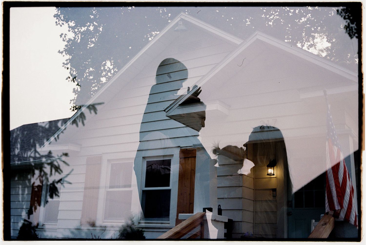 A white house exterior with multiple windows and a gable roof in a double exposure on film.