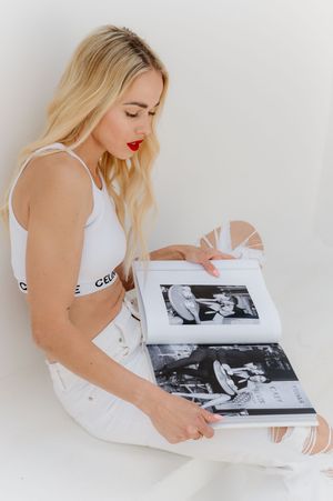 A person in white attire sits looking through a photo album or portfolio containing black and white photographs.