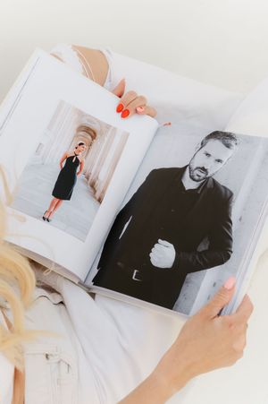 Someone holds a photo album showing black and white photographs, with bright red nail polish visible on their fingers.
