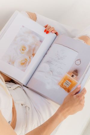 Someone holds open a lifestyle magazine showing elegant white roses and perfume bottle on its pages.