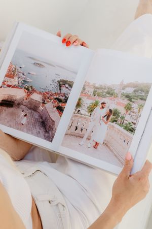 Hands holding open a photo album showing scenic travel photographs of red-roofed European city landscapes.