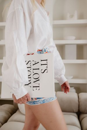 White oversized sweatshirt with text print and decorative detail shown against neutral built-in shelving.
