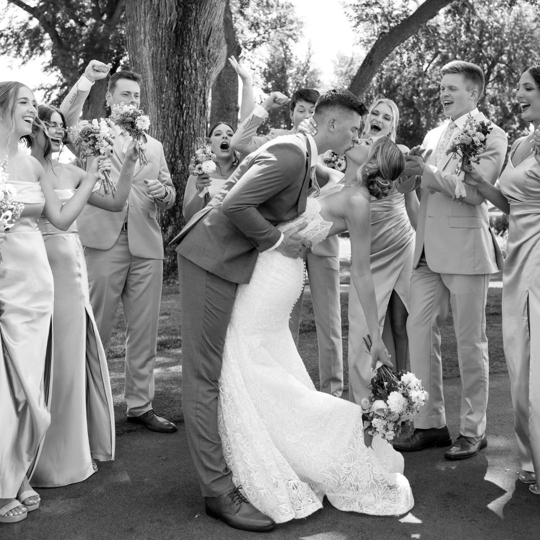 Wedding celebration with guests cheering outdoors under trees.