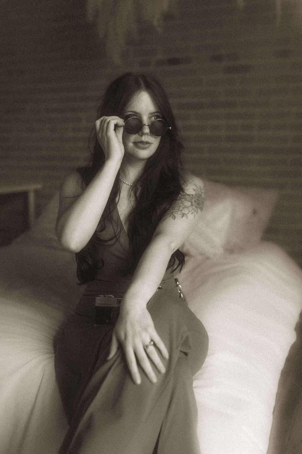 Black and white sepia portrait of someone in a dark dress and sunglasses posing on a light-colored couch.