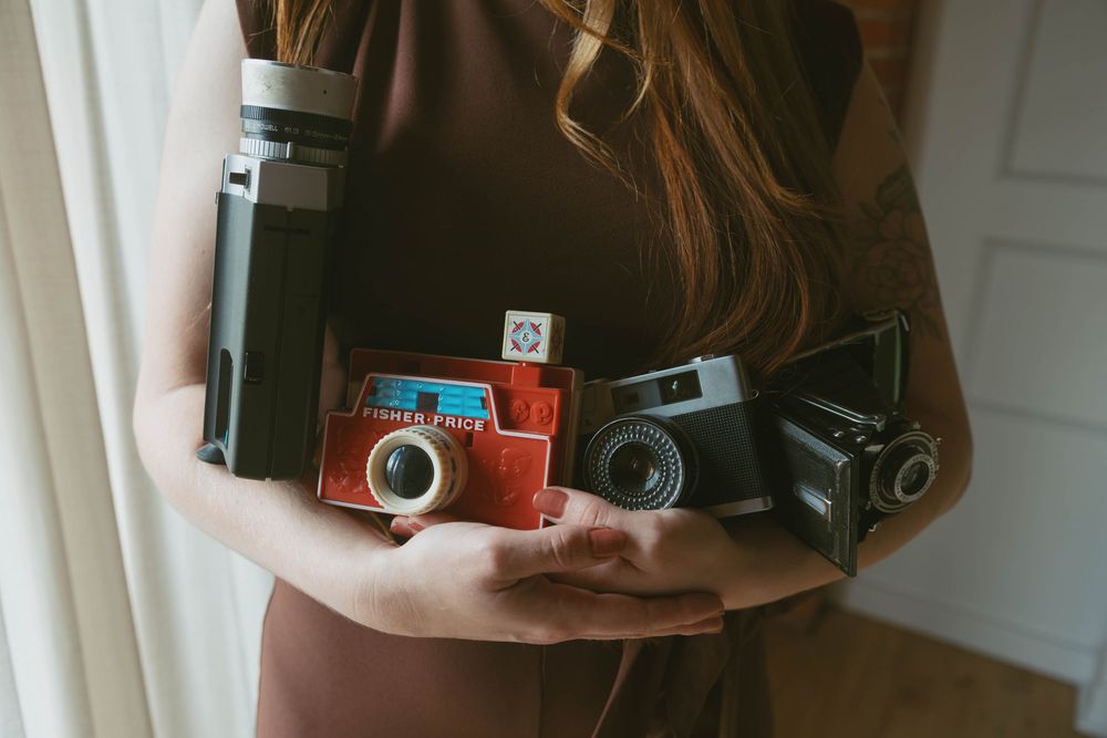 Woman holding a collection of vintage cameras including film and instant models in her hands.