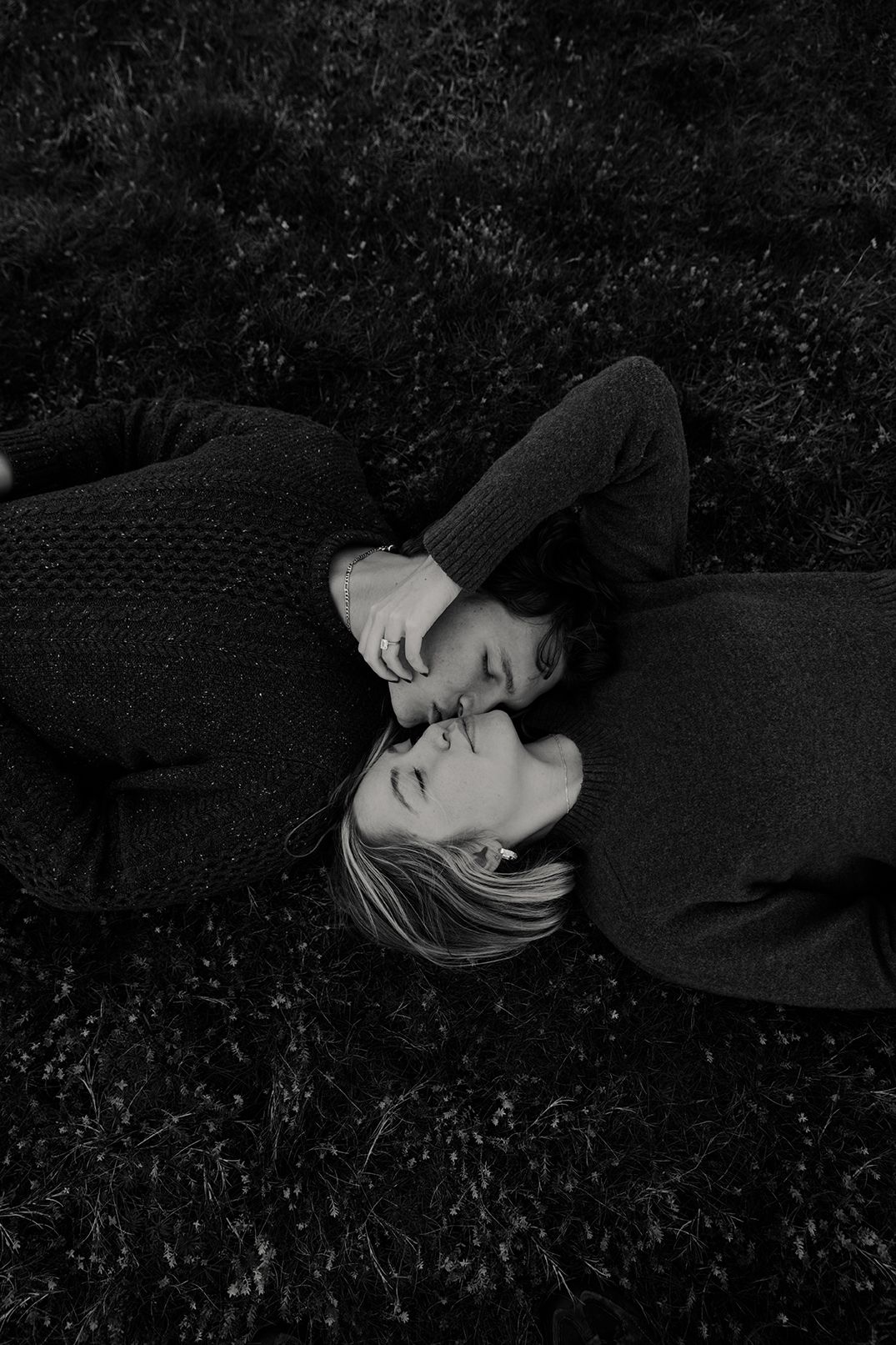 a couple laying on the grass next to each other and kissing one another