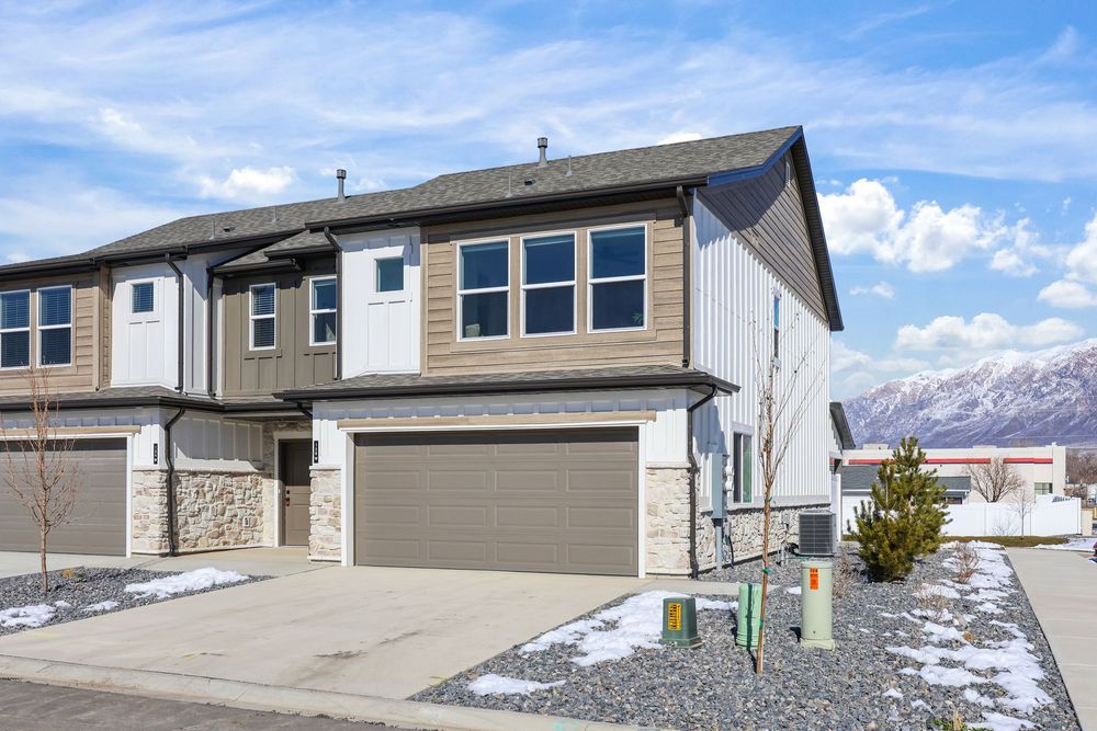 Two-story townhome with tan siding, stone accents, two-car garage, and mountain views in winter. Captured by Slate Media (best in UT)