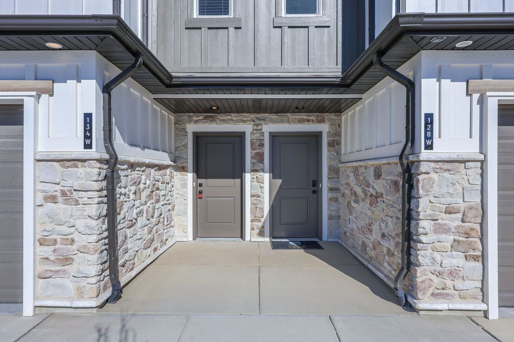Close-up of townhome entryway featuring stone columns, board and batten siding, and gray front door. Captured by Slate Media (best in UT)
