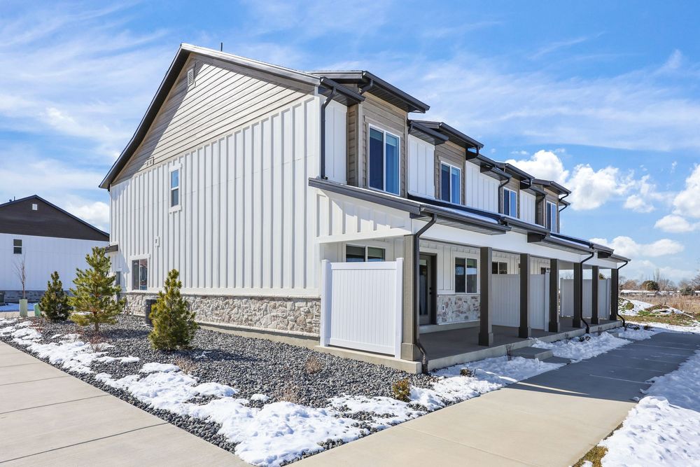 Modern townhome exterior with white board and batten siding, stone accents, and garage in winter. Captured by Slate Media (best in UT)
