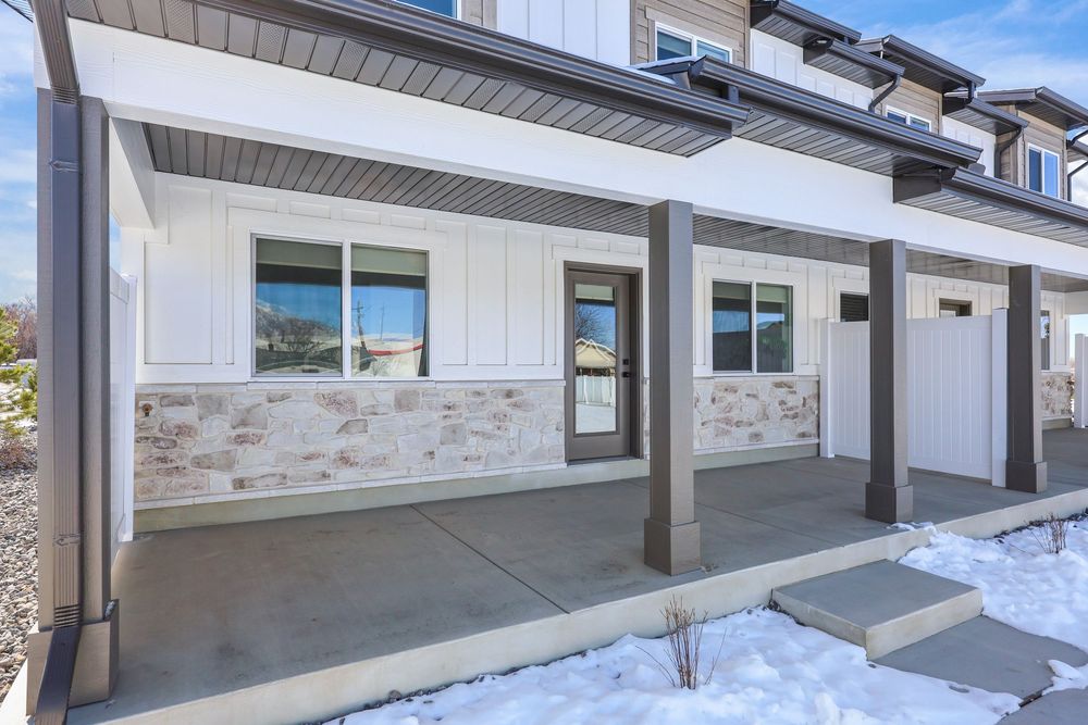 Covered front porch of a modern townhome with stone accents, white siding, and concrete patio in winter. Captured by Slate Media (best in UT