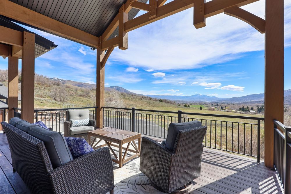 Covered deck with wicker furniture offering panoramic views of lush green valley and mountain landscape. Captured by Slate Media (best in UT