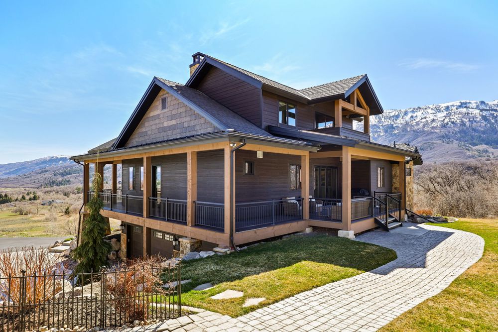 Mountain craftsman home with wraparound porch, wood siding, stone accents, and scenic valley views. Captured by Slate Media (best in UT)