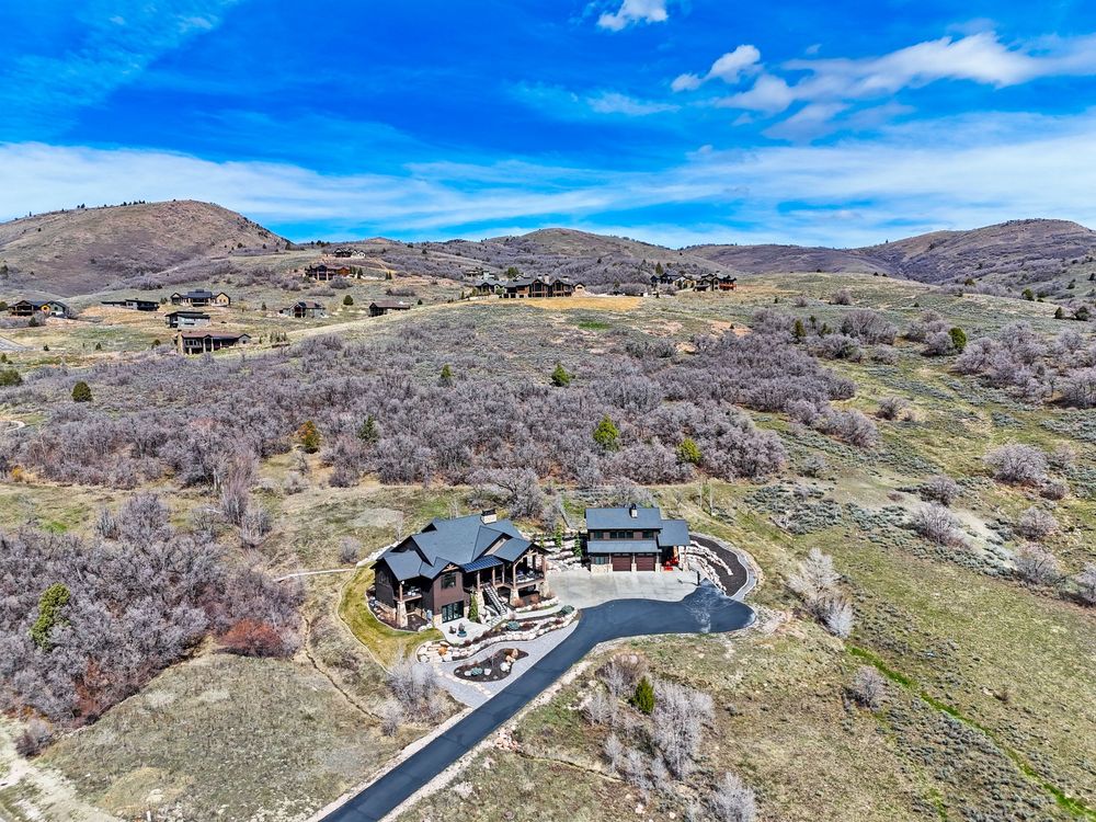 Aerial view of craftsman mountain home with circular driveway nestled among natural brush and rolling hills. Captured by Slate Media