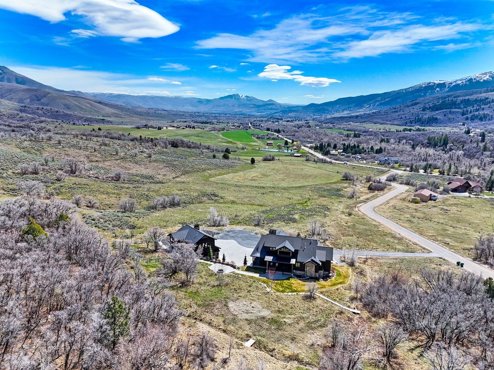 Aerial view of a rural mountain home surrounded by sagebrush with sweeping valley and mountain views under blue skies.