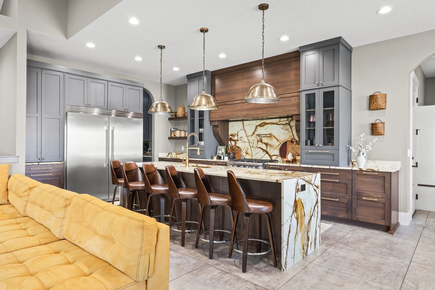 Elegant kitchen with gray cabinets, wood accents, marble waterfall island, and leather bar stools. Captured by Slate Media (best in UT)