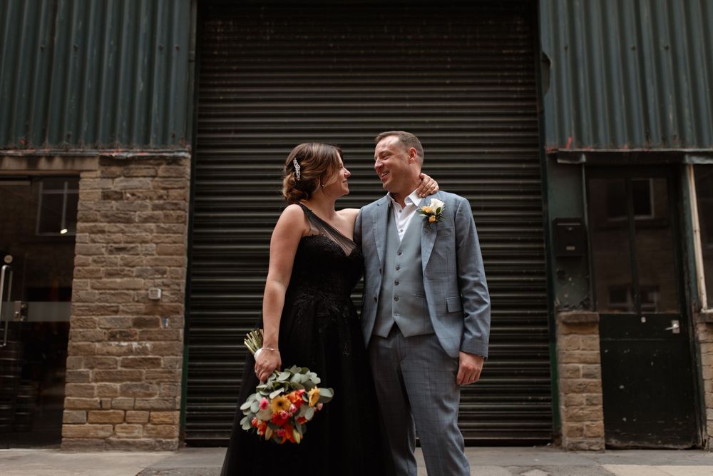 A newlywed couple sharing an intimate moment against an industrial backdrop with brick and metal doors.
