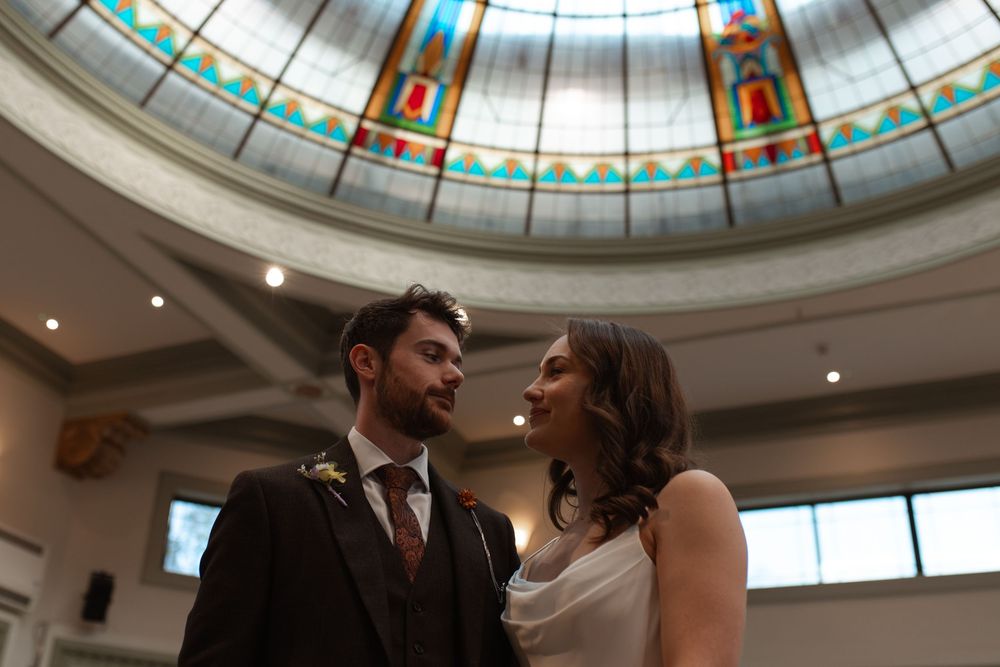 A happy couple shares an intimate moment under a grand domed ceiling with stained glass details and soft lighting.
