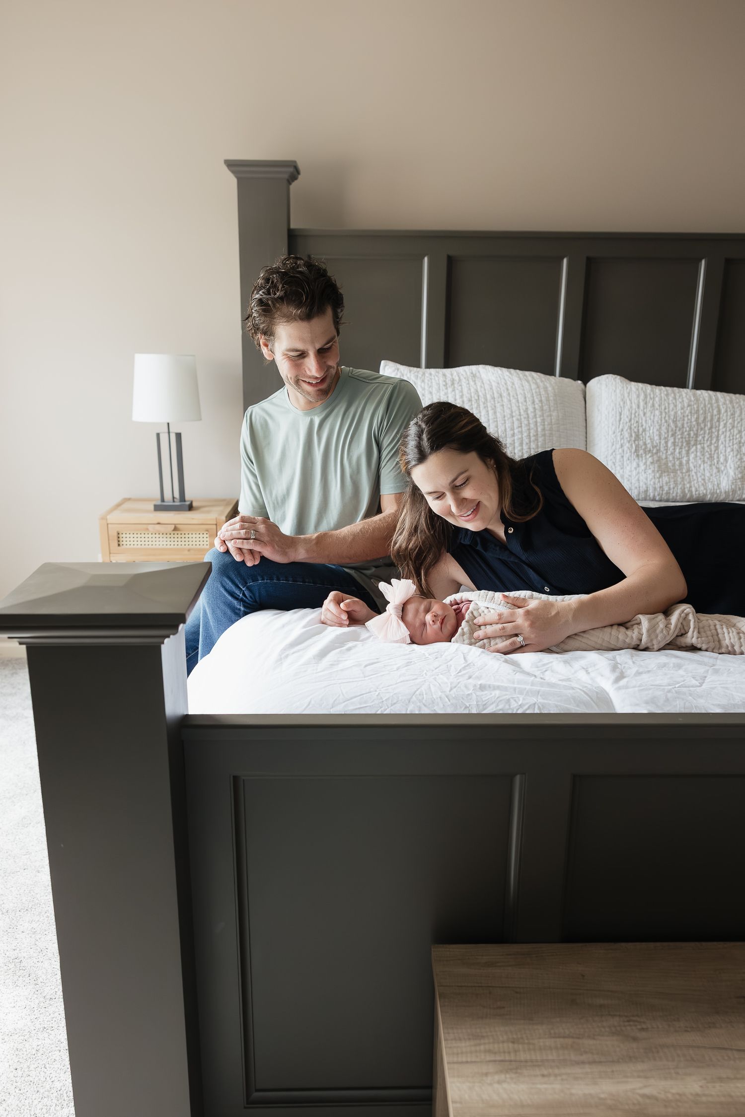 new parents sitting and laying on master bed with newborn baby girl Family Photographer Kansas City