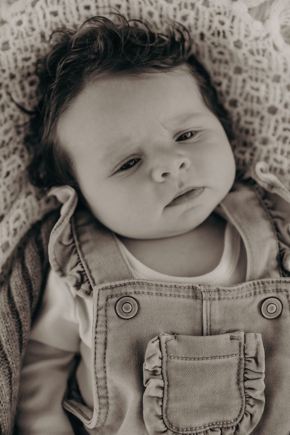 Black and white close-up portrait of a newborn baby in denim overalls looking up.
