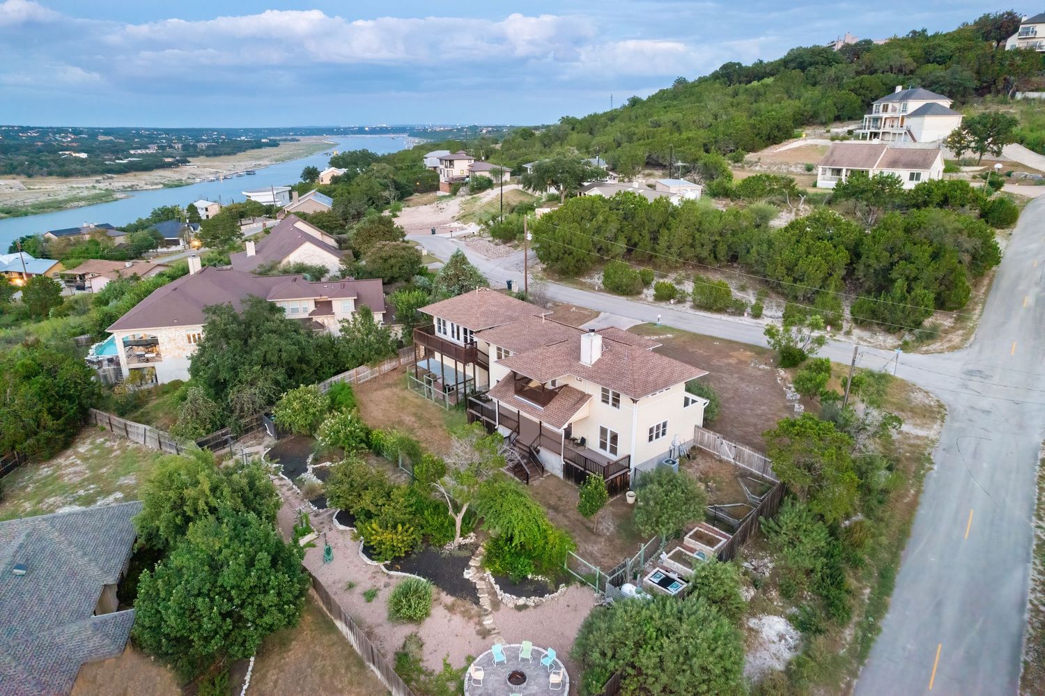 Aerial view of luxury homes nestled on a hillside overlooking Lake Travis with lush landscaping and winding roads.