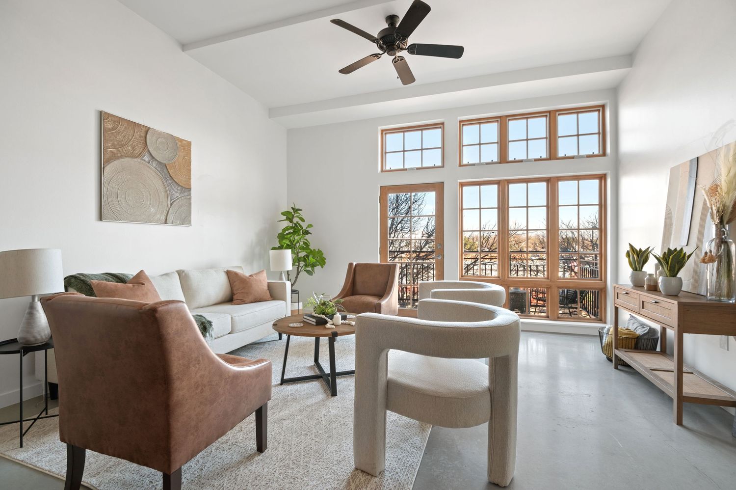 Modern living room with brown armchairs, white walls, and large windows overlooking a balcony.