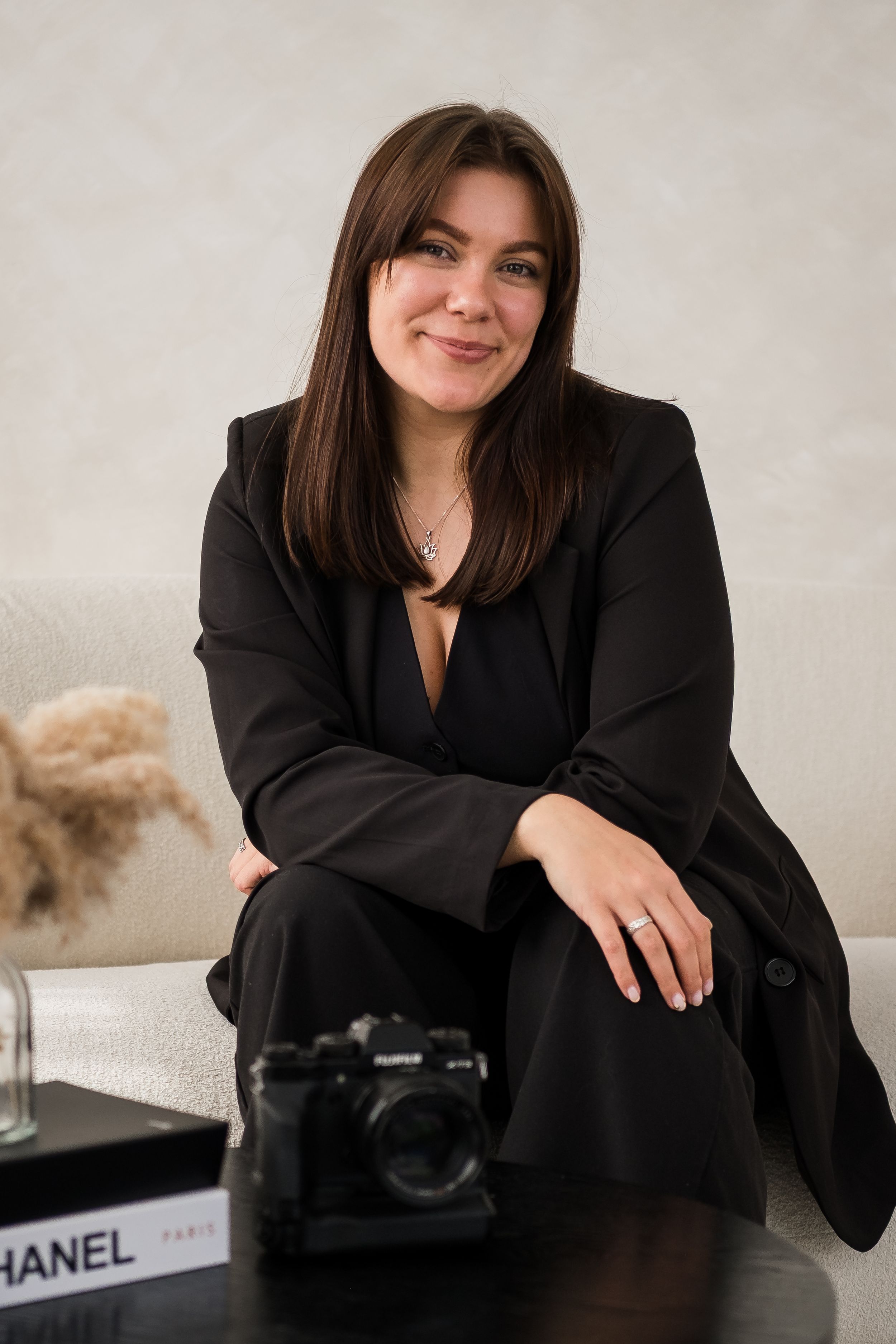 Professional headshot portrait with warm smile wearing black sweater and white shirt against neutral background.