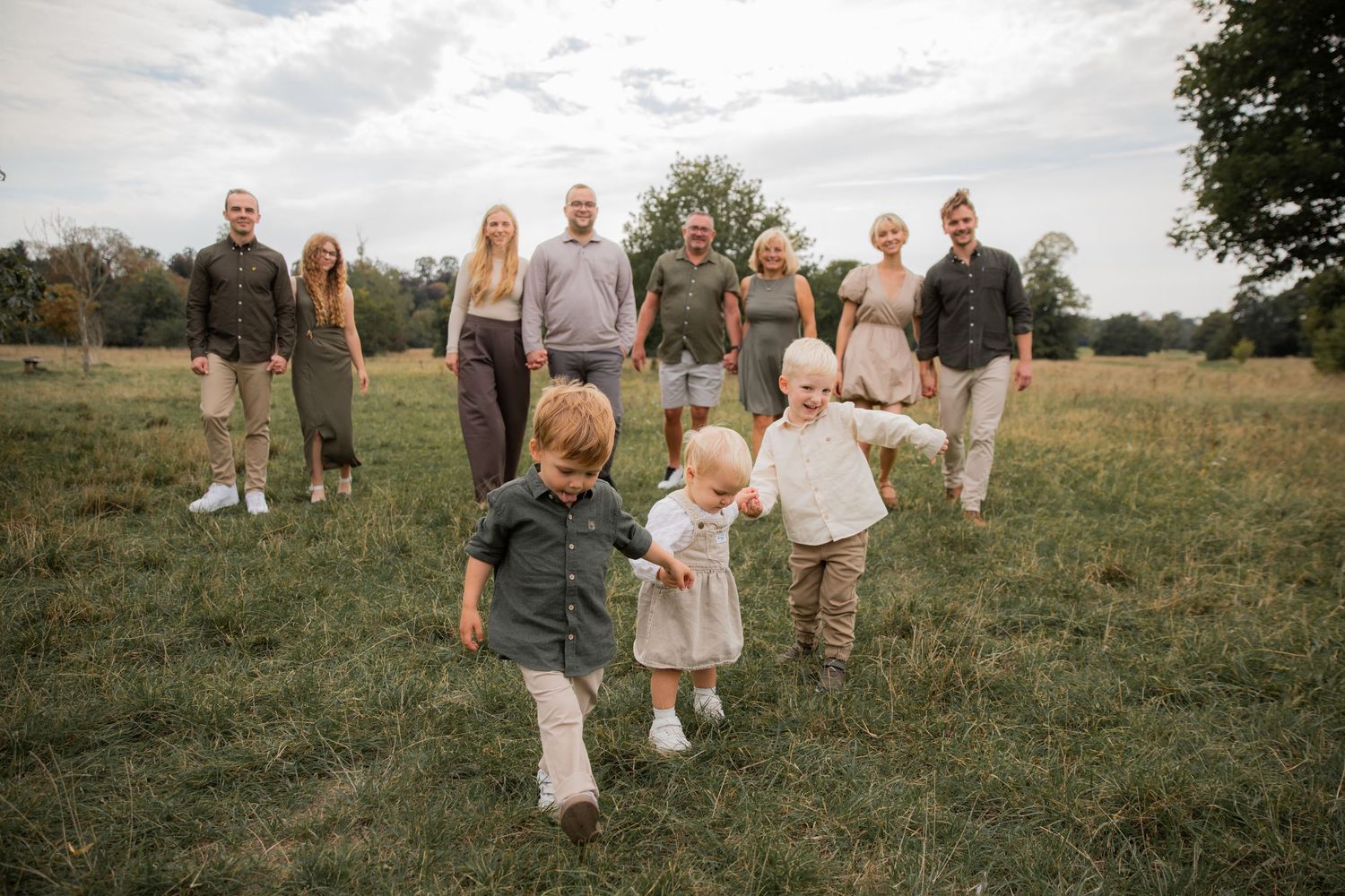 A family group in coordinating neutral outfits poses together in a sunlit grassy meadow during golden hour.