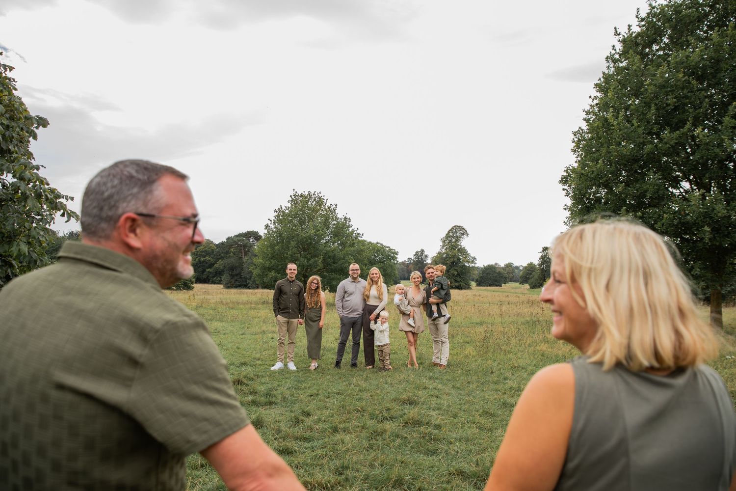 People gather in a grassy field on a sunny day, with some standing and others sitting on the ground.