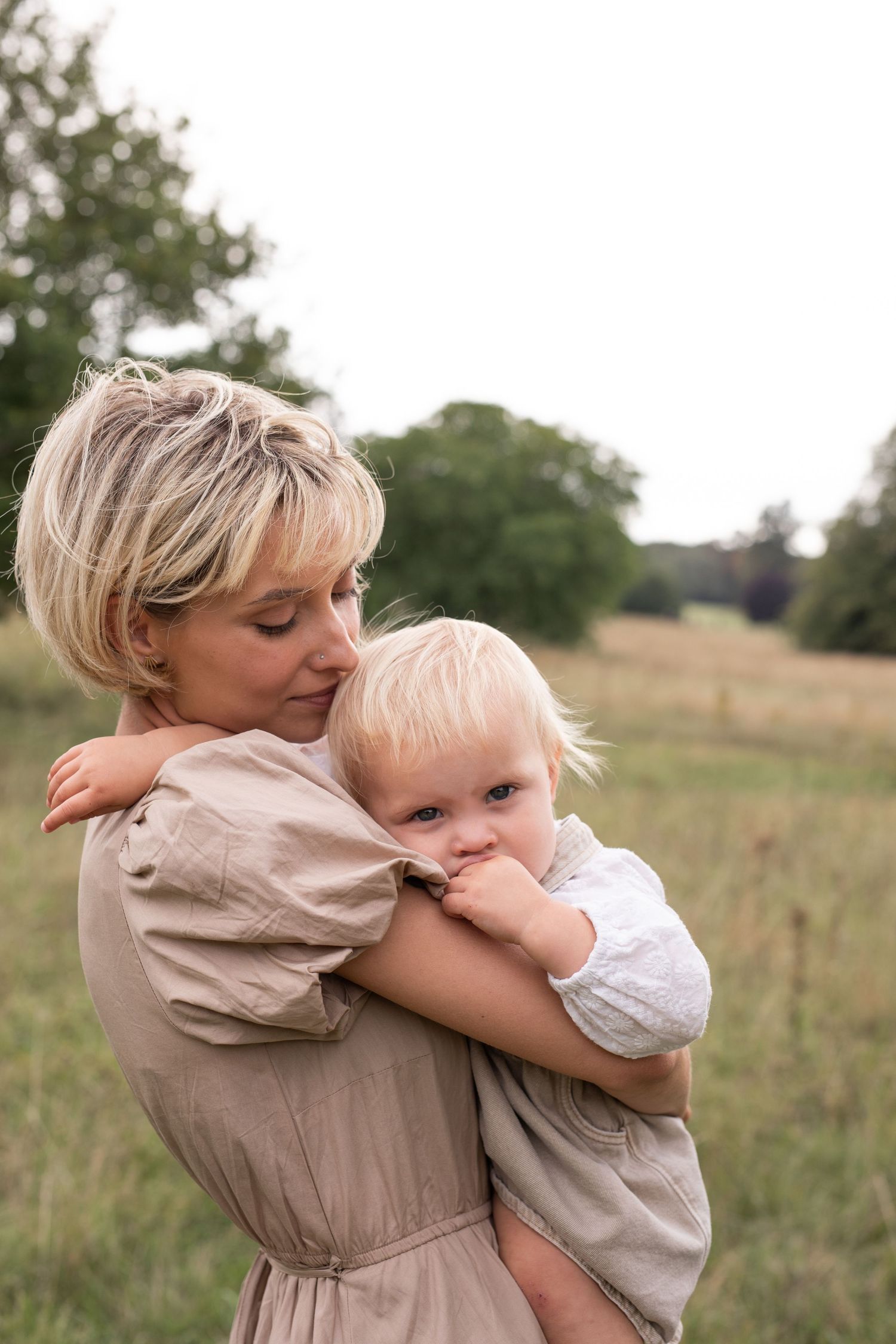 A series of tender embraces between parent and child in a sunlit meadow with tall grass and trees in the background.