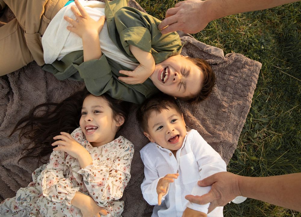 A sequence of candid outdoor photos showing joyful laughter and playful moments on the grass.