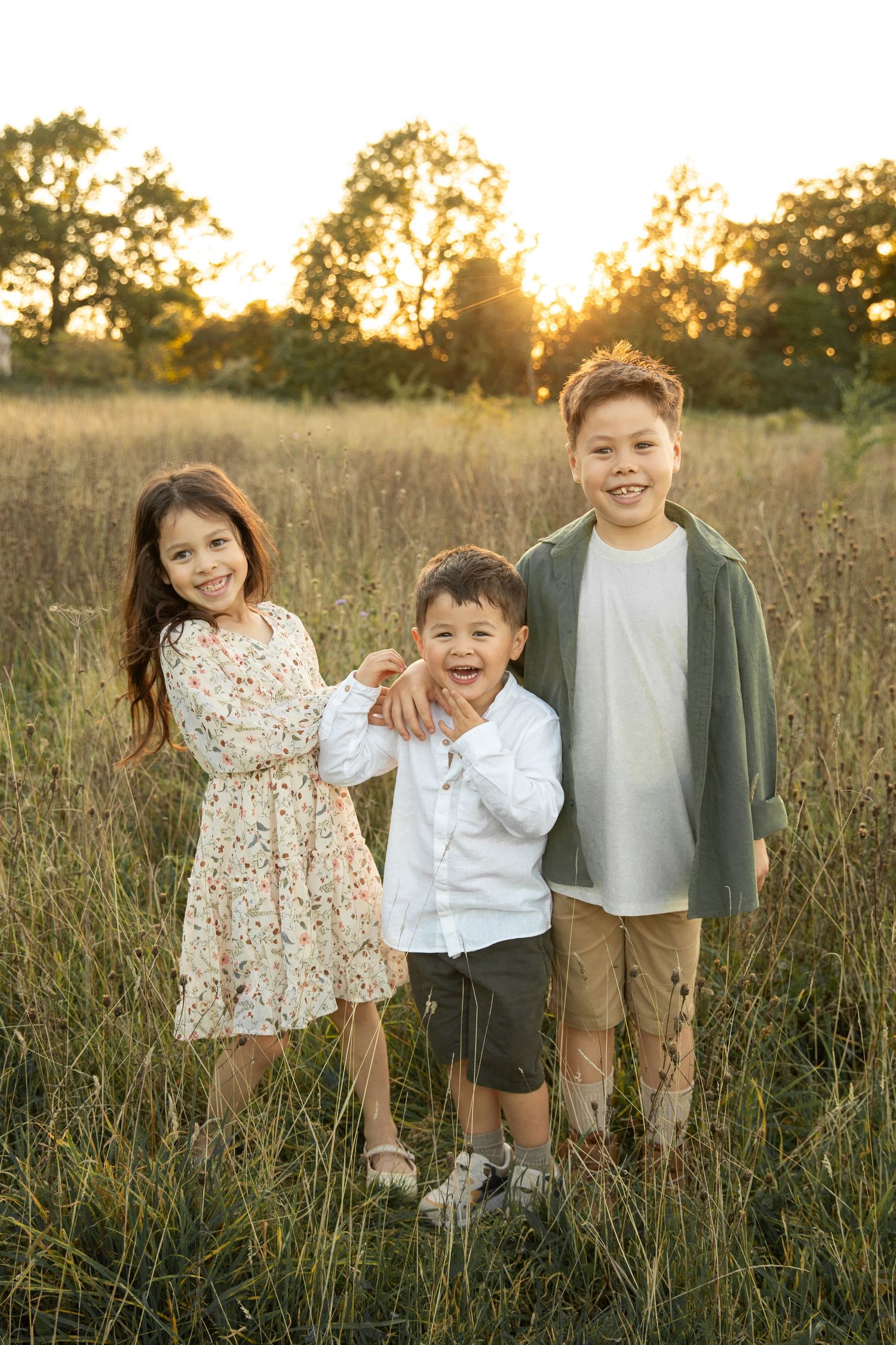 Children playing together in a golden sunlit meadow during sunset with tall grass and trees in the background.