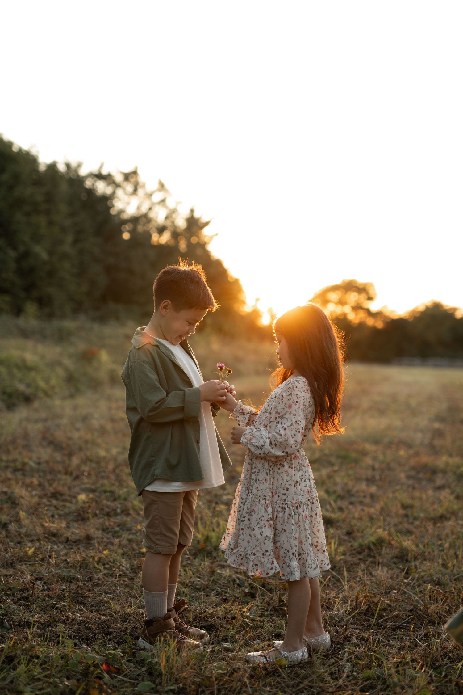 Two children play together in a grassy field at sunset creating a magical golden hour moment.