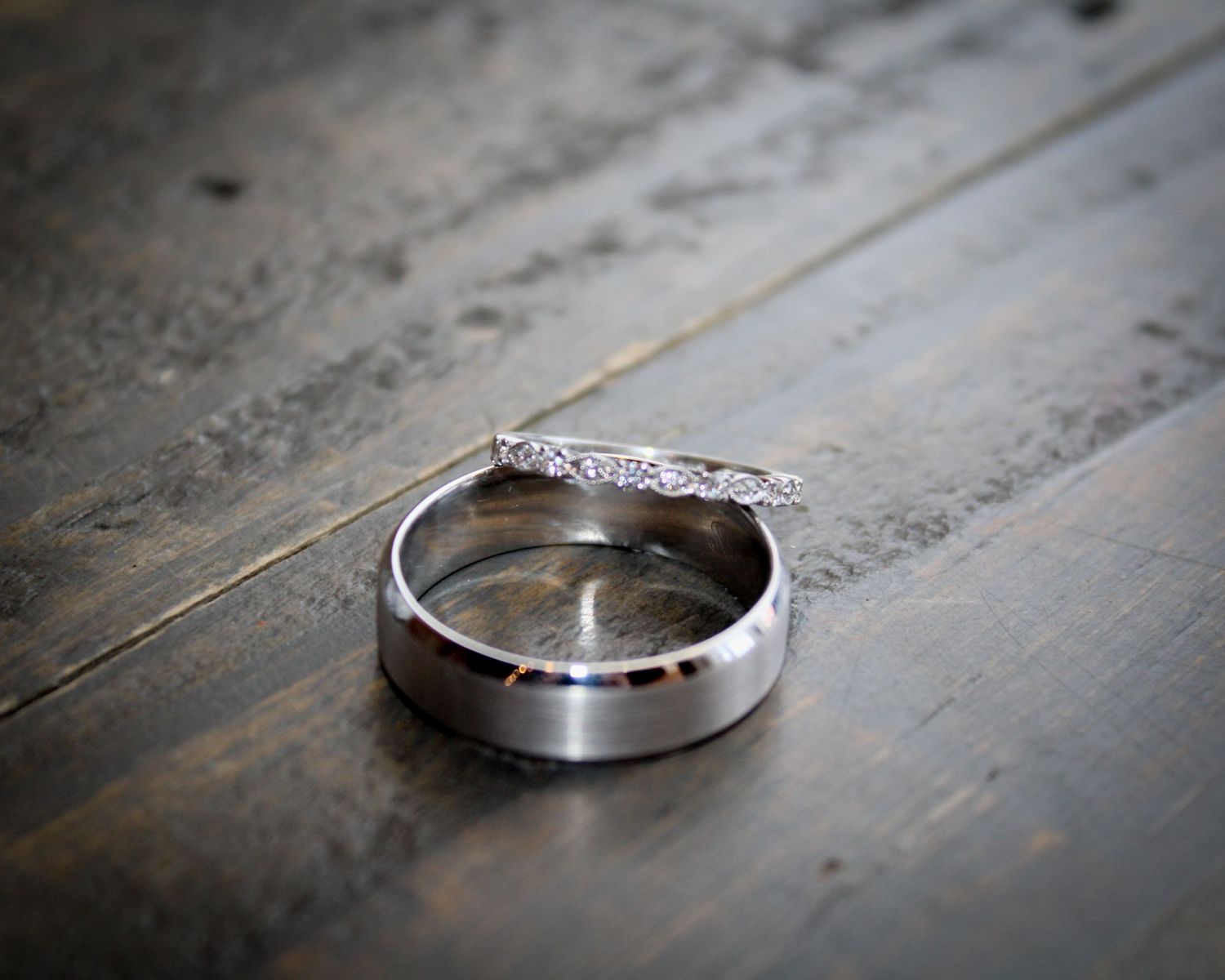 Wedding rings photographed in dramatic lighting on a dark wooden surface.