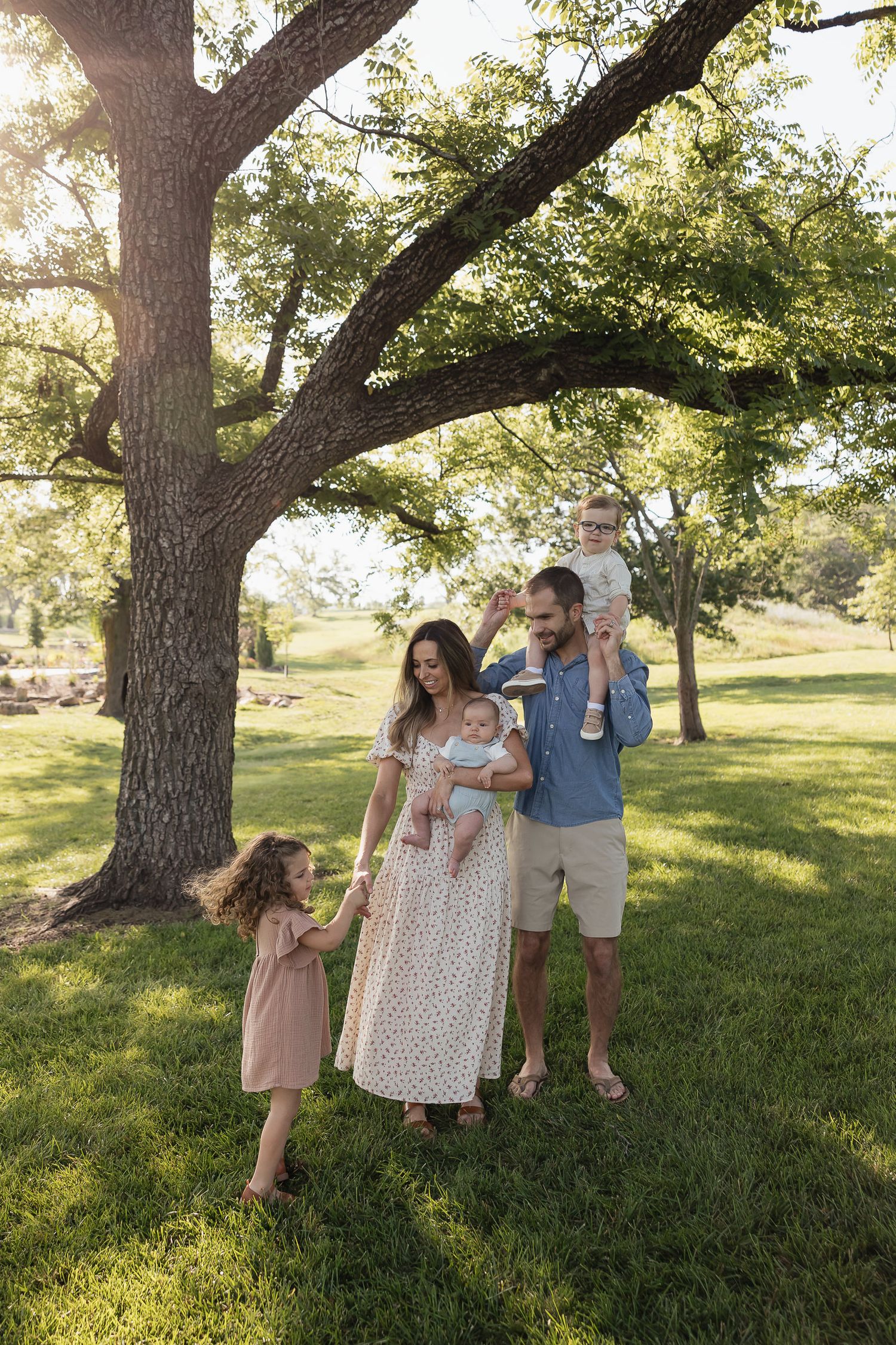 family of five dancing under a big oak tree at lake olathe with green grass and three smiling children