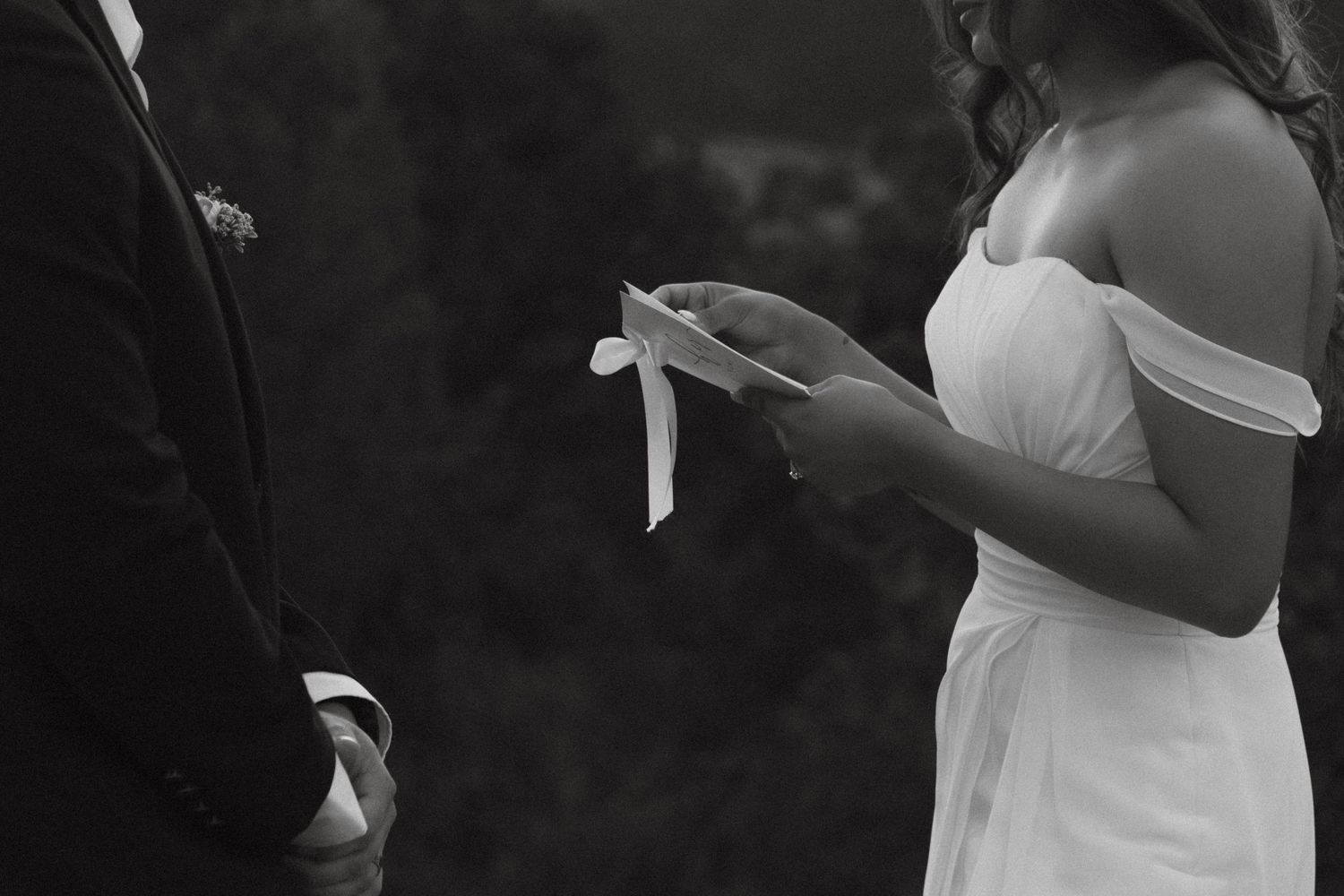 Black and white wedding ceremony photo showing couple exchanging vows and reading from paper during elopement ceremony in Colorado