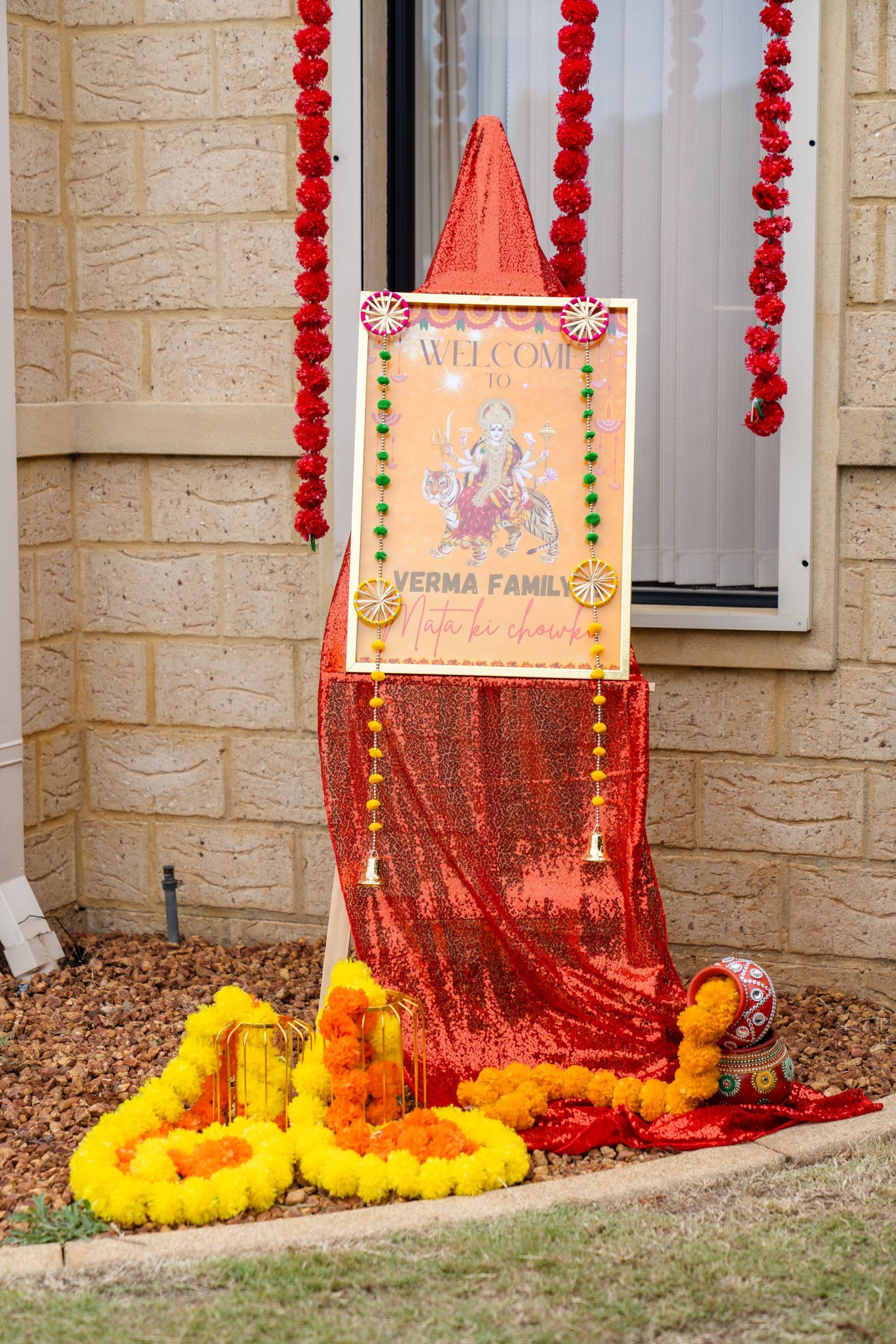 Decorative red beaded garlands and marigold flowers adorn a home entrance with a welcome sign for Diwali celebration.