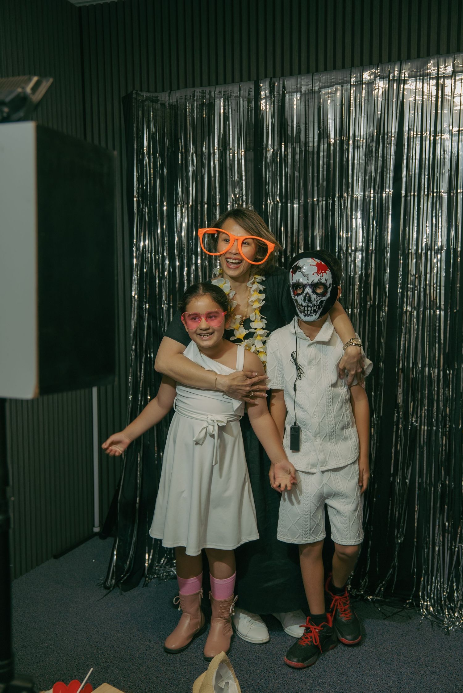 Three people pose together against a silver tinsel backdrop at a party with fun costume accessories and outfits.