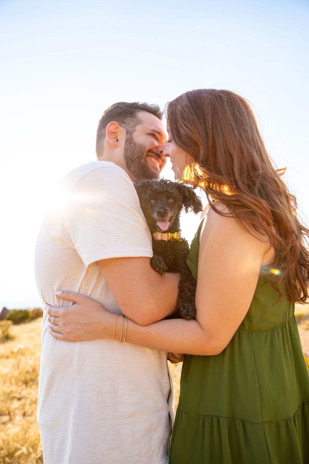 A couple embraces in a golden sunlit field, the woman wearing a dark green dress and the man in white.
