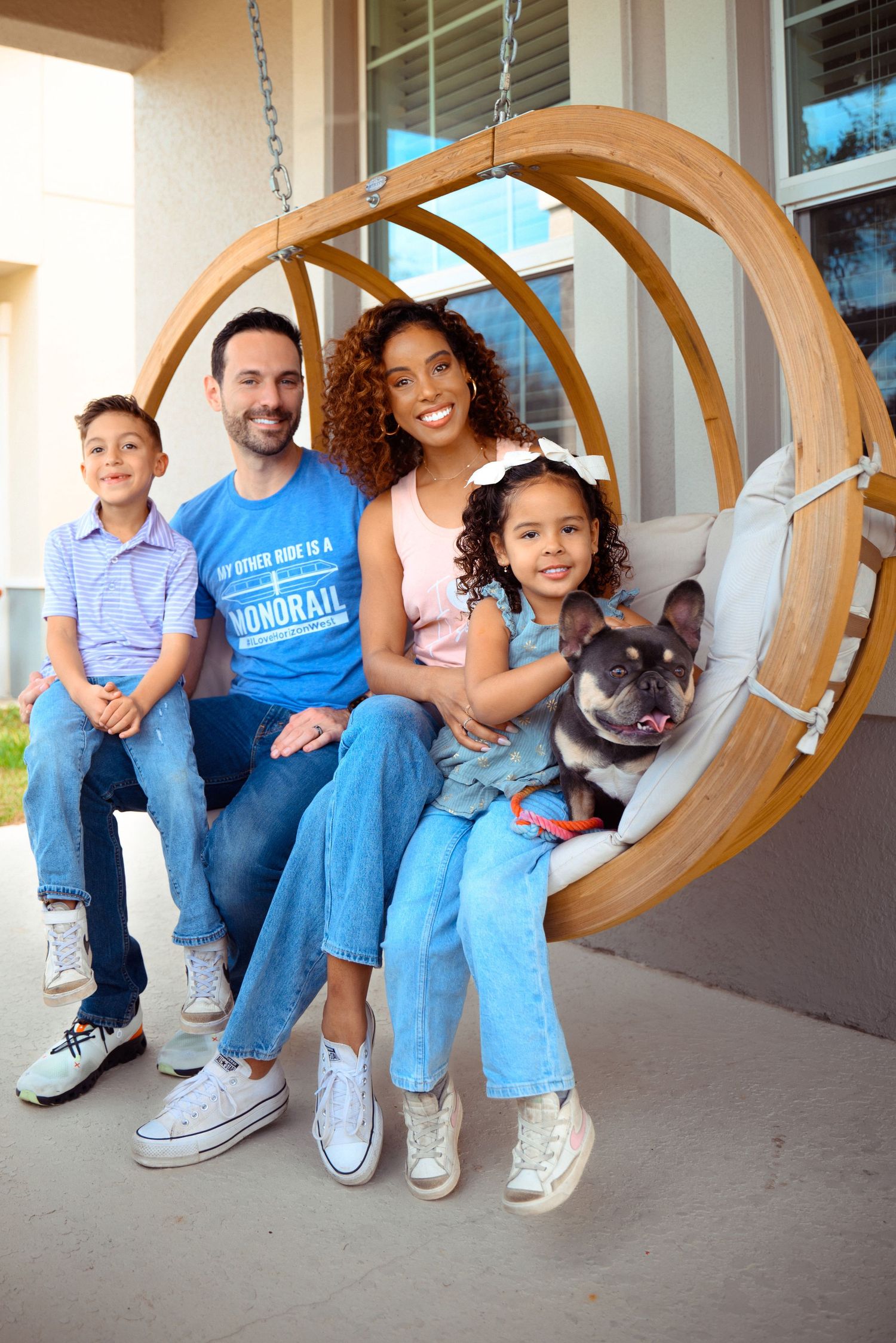 Family sitting together on a curved wooden porch swing with their French Bulldog pet.