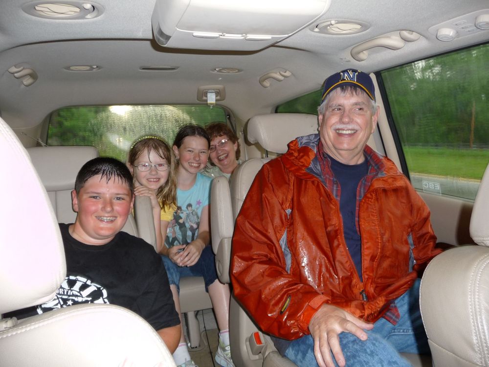 Family road trip scene inside SUV with passengers smiling at camera.
