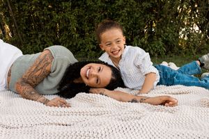 Mother and young son laughing together while lying on a white knit blanket outdoors.