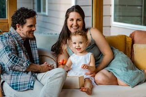 Happy young family with smiling toddler poses together on a cozy porch setting.