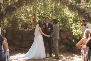 Bride and groom exchange vows at outdoor woodland wedding ceremony with guests seated.