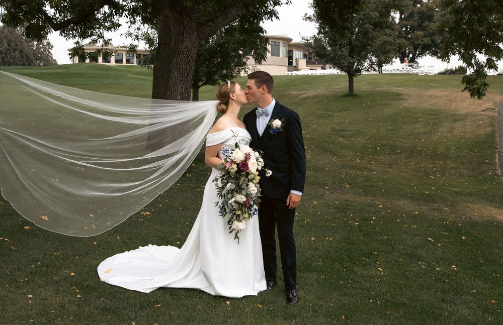 Bride and groom kiss outdoors as her long veil flows dramatically in the wind.