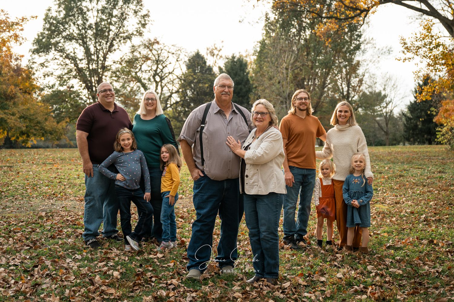 A group stands together on fallen autumn leaves in a park setting during golden hour.