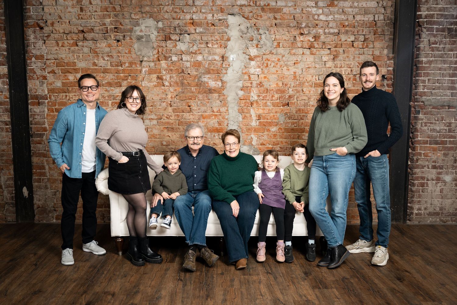 Group stands together against rustic brick wall backdrop on wooden floor in coordinated casual attire.