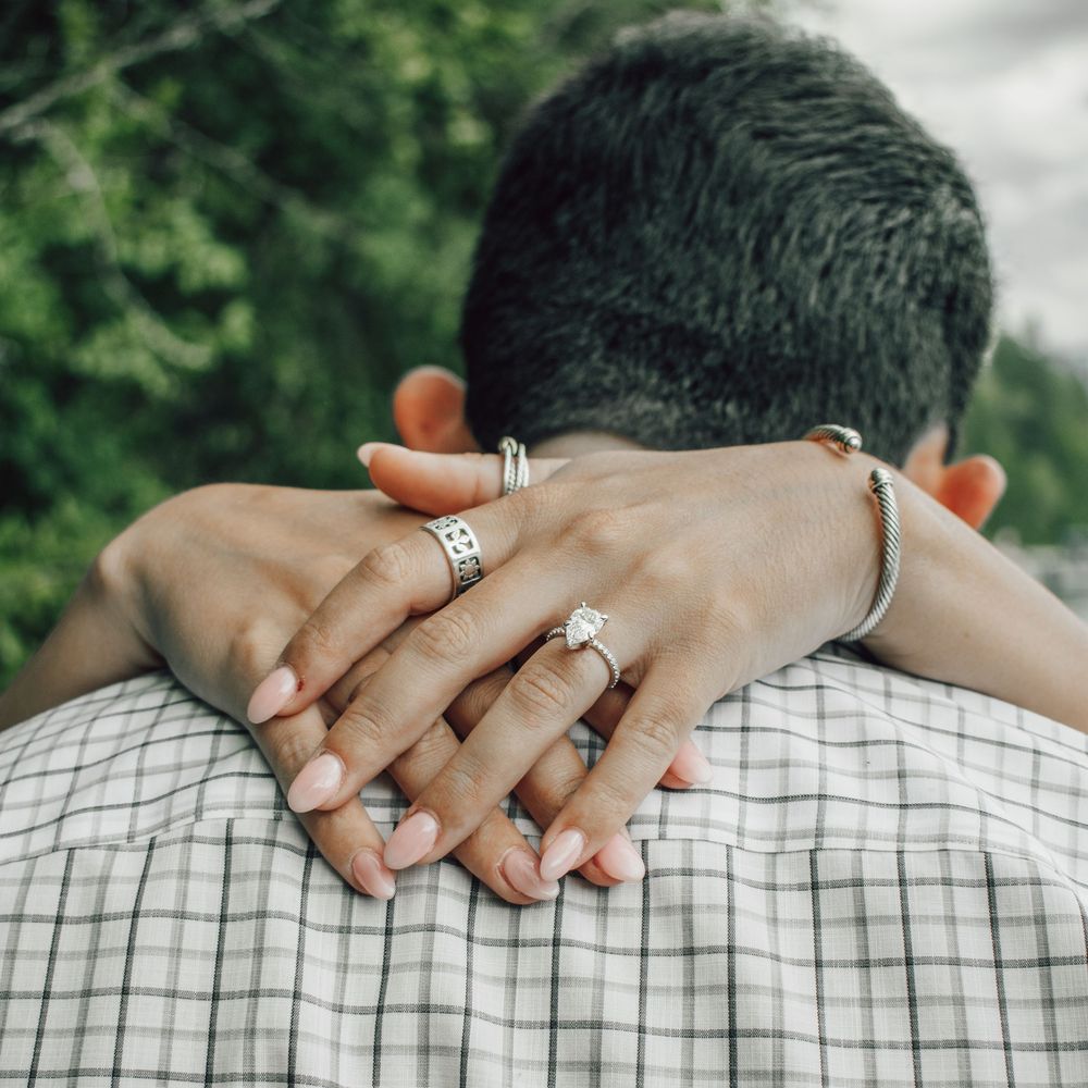 Close-up of a woman's hands with an engagement ring resting on a man's shoulders during an embrace.