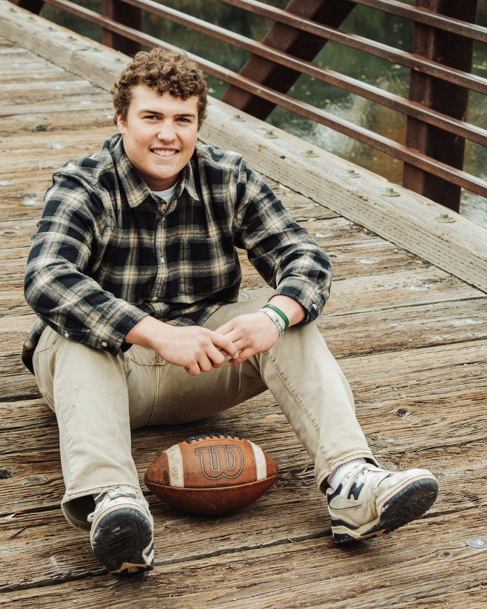 Senior portrait session featuring casual poses with football on rustic wooden deck.