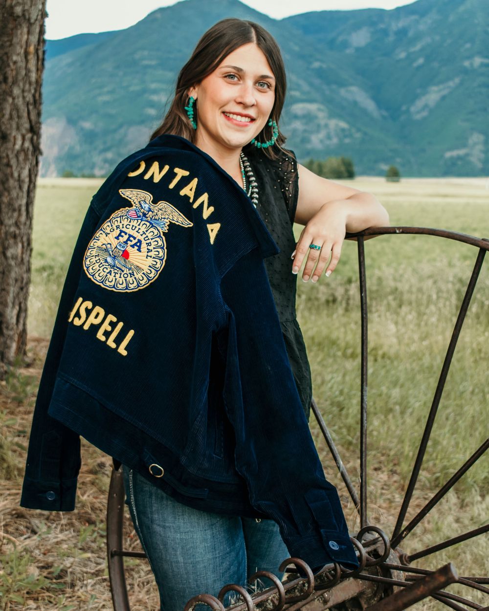 A rustic outdoor portrait session featuring a navy letterman jacket against a mountain landscape backdrop.
